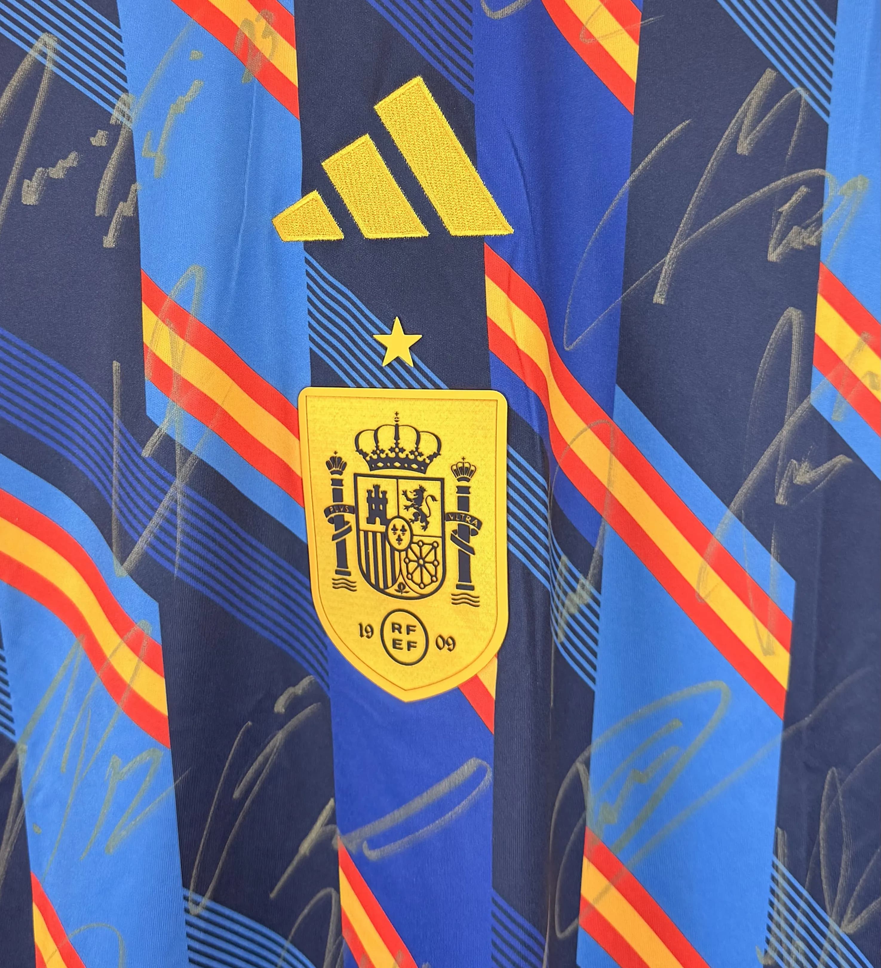 announcements/9deaa2e2-a6e2-46d0-9b2f-1a2ad64684fb/1785366782812-Camisa-Aquecimento-Espanha-Copa-2026-Autografada-Elenco-Campeao-Detalhe.webp