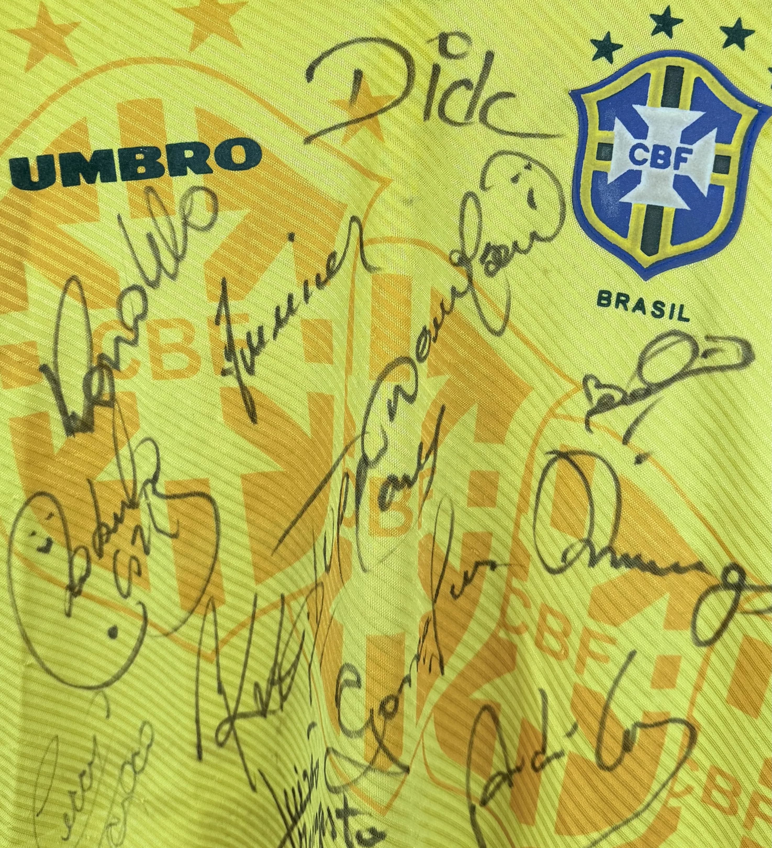 announcements/a1933fbb-8a22-41cf-9759-cc950f446541/1785365426660-Camisa-Brasil-1995-Autografada-Elenco-Ronaldo-Detalhe.webp