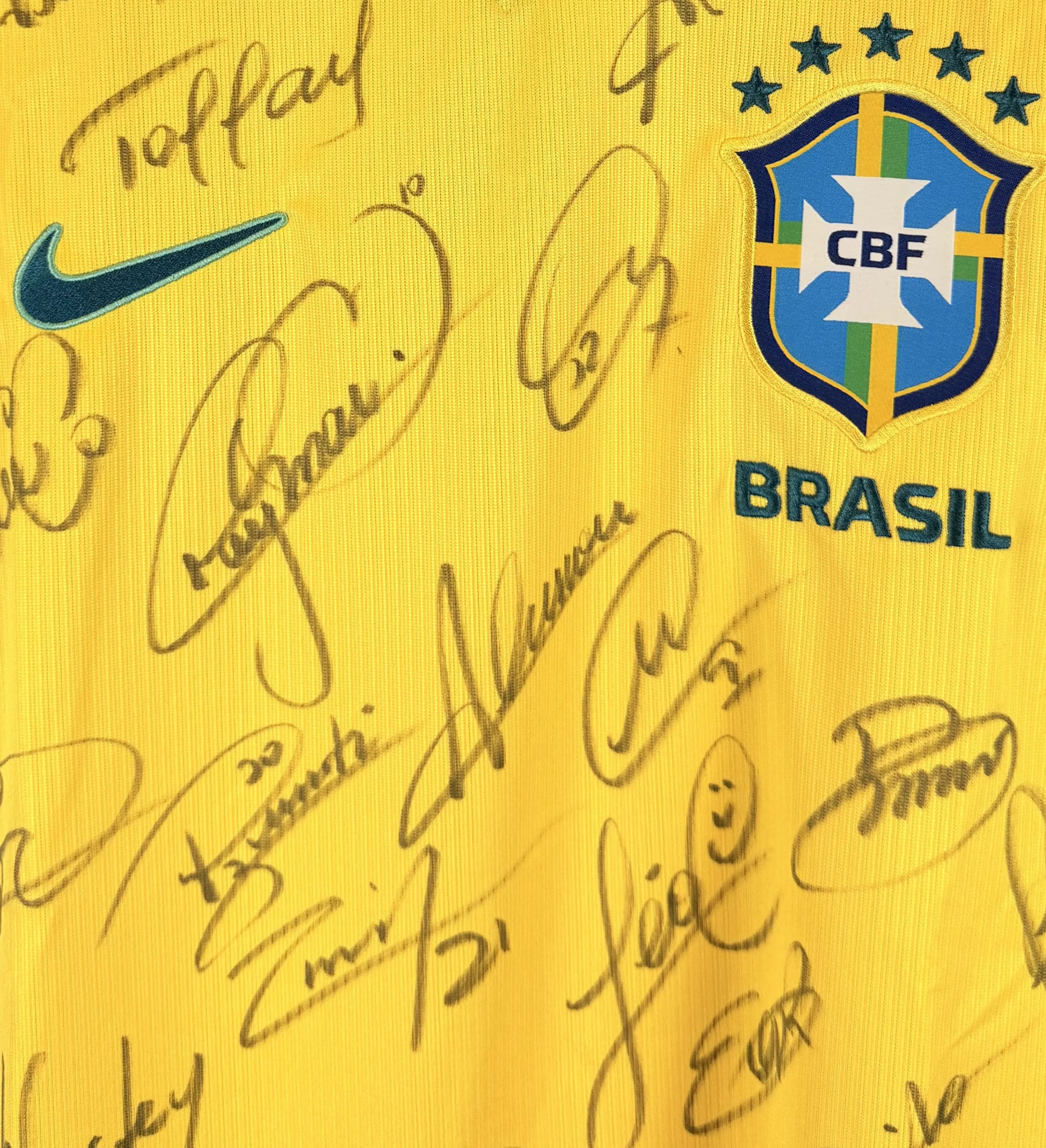 announcements/a1cb4d1e-bbf8-4f49-8445-ad4f149a37e6/1785343940678-Camisa-Brasil-Amarela-Copa-2026-Autografada-Elenco-Neymar-Detalhe.webp